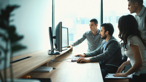 Closeup side view of group of young IT experts completing a task, a part of their daily routine at IT company. There are three men and a woman.