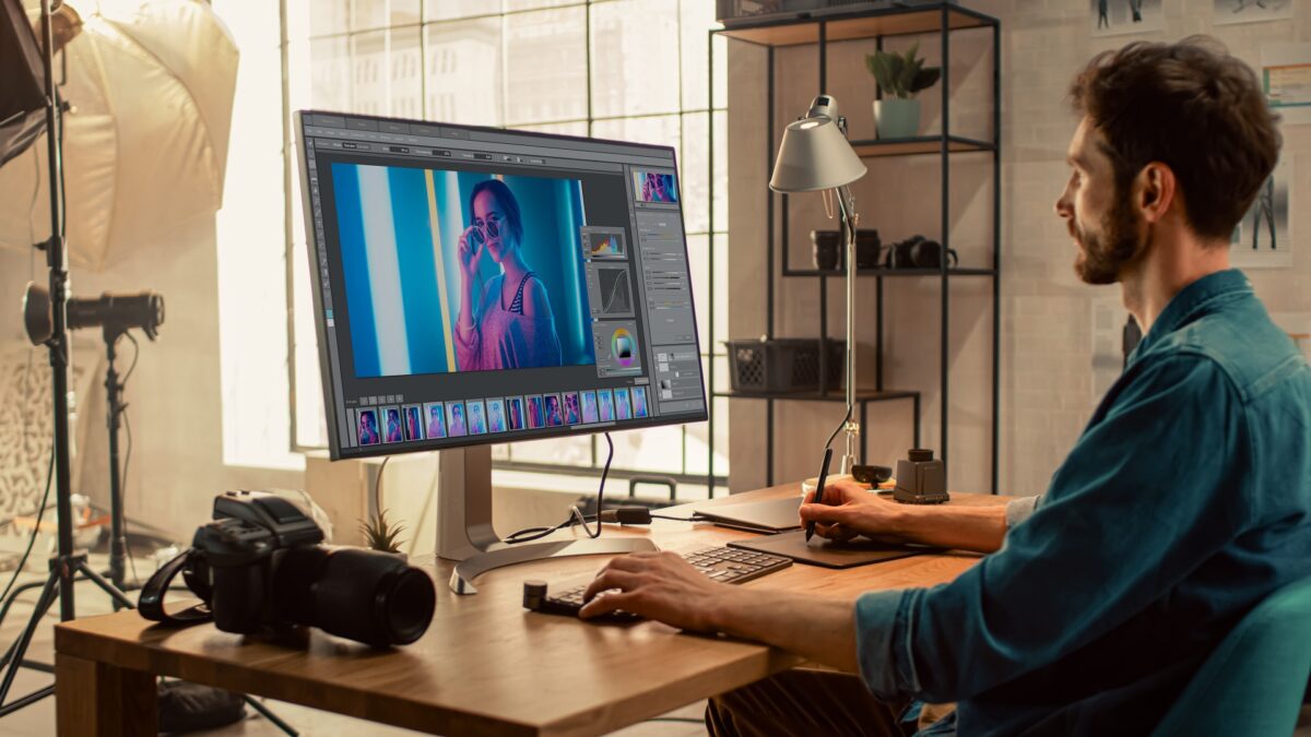 Professional Photographer Sitting at His Desk Uses Desktop Computer in a Photo Studio Retouches. After Photoshoot He Retouches Photographs of Beautiful Female Model in an Image Editing Software