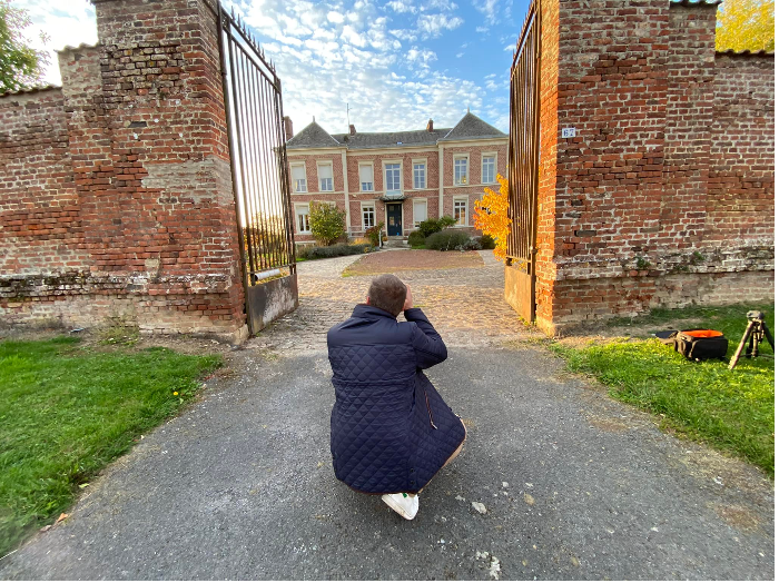 back of a man crouching to take a picture of a fancy house