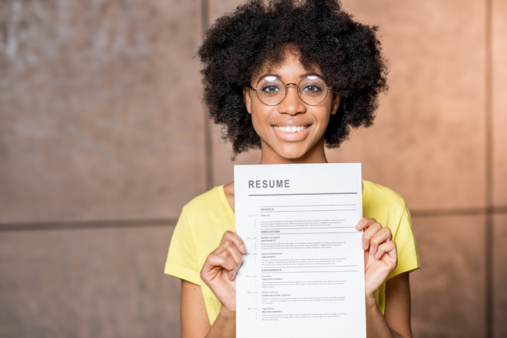 Une femme regarde l'objectif en tenant son CV dans la main
