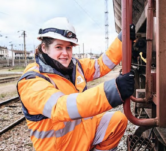 Une jeune femme casquée en tenue professionnelle monte dans la cabine de pilotage d'un train