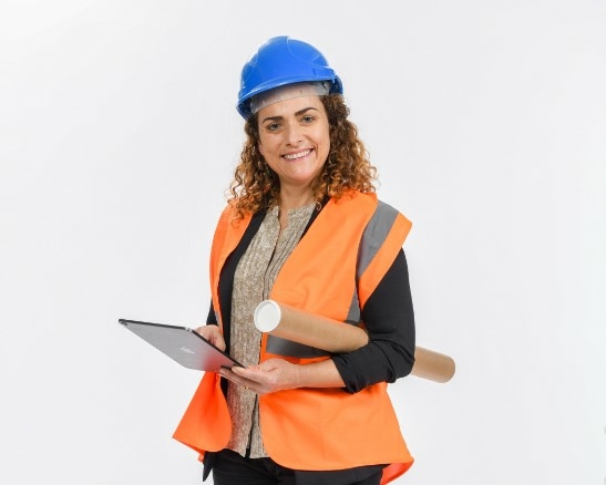 Une technicienne du bâtiment avec casque, gilet orange, et tablette numérique