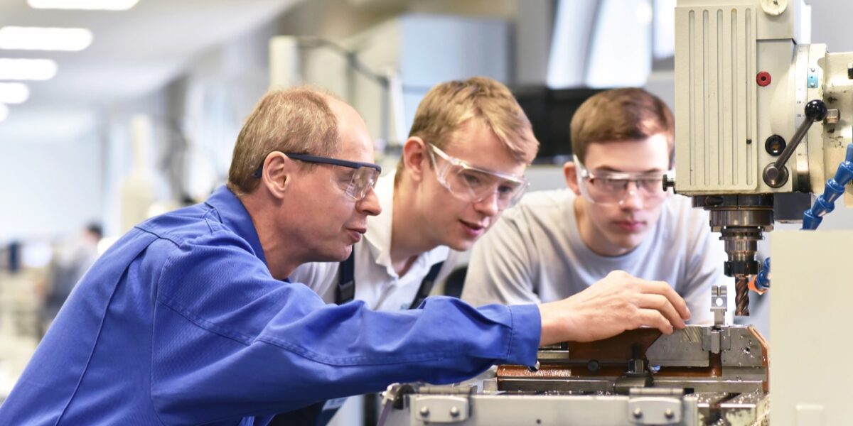 deux apprentis et leur tuteur utilisent une machine