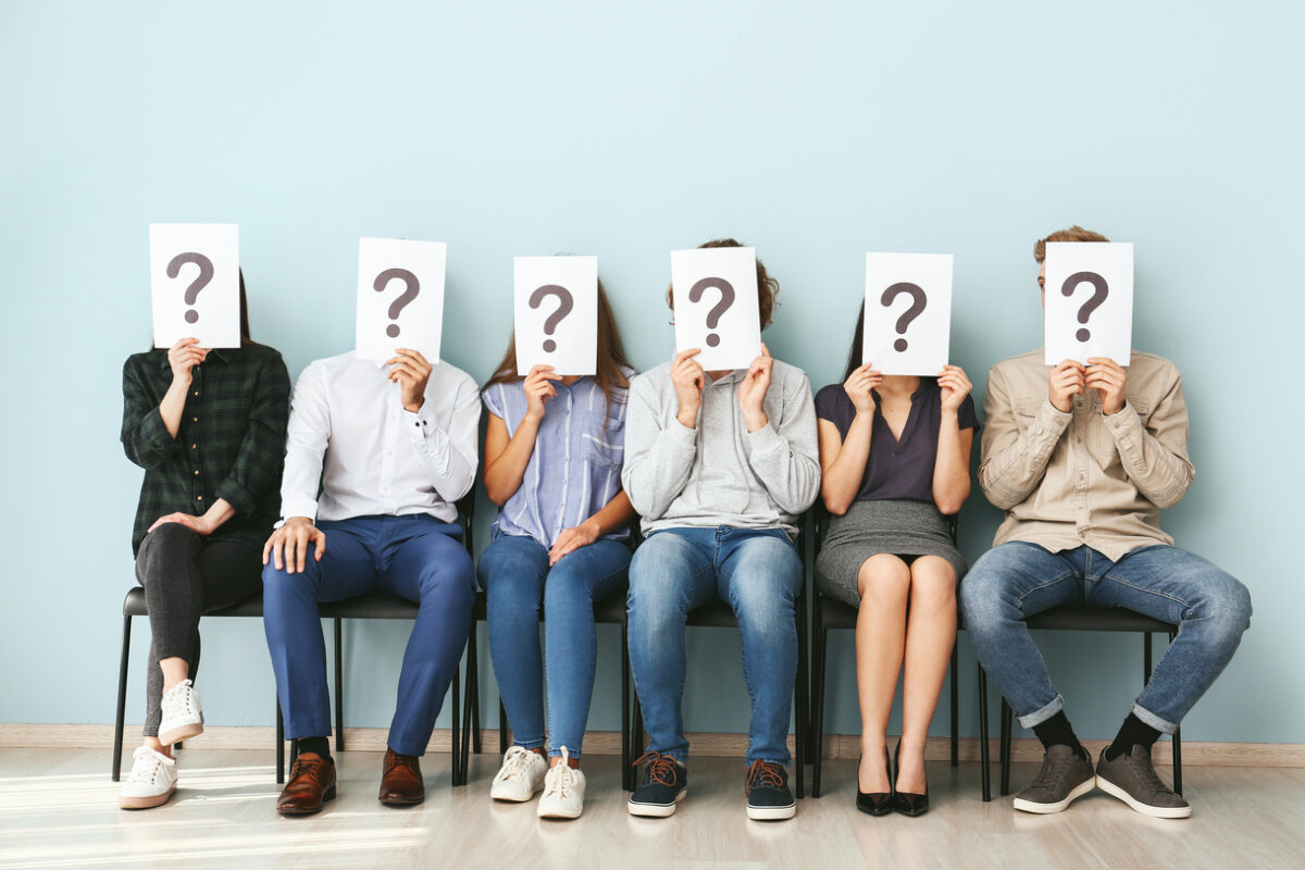 Young people hiding faces behind paper sheets with question mark