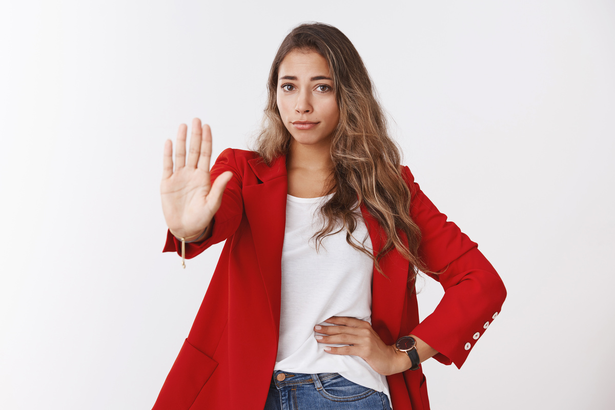 No means never. Portrait disappointed unimpressed confident young 25s caucasian curly-haired woman wearing red jacket extending palm stop, refusal gesture, restraining, rejecting offer disliking it