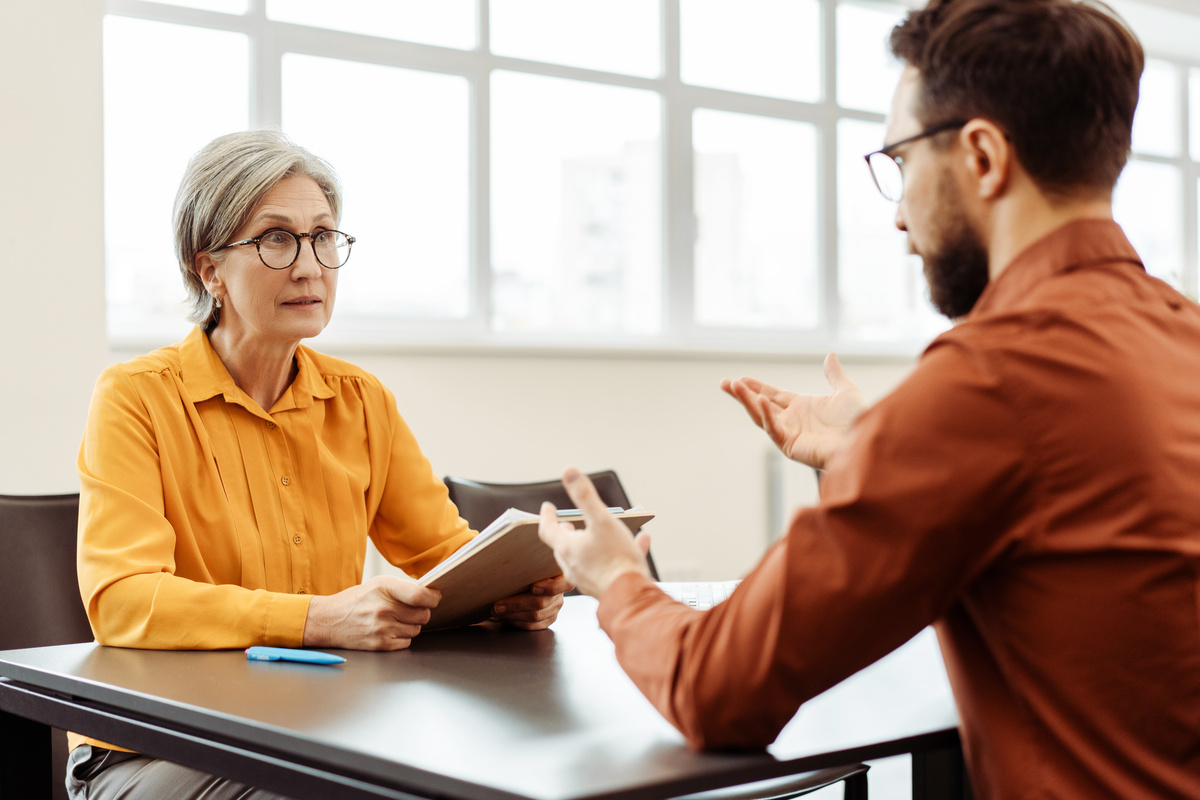 Serious senior business woman, employer holding resume listening  candidate at job interview. Team business people talking, meeting, sharing ideas sitting n modern office. Human resources concept