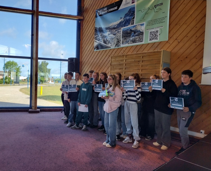 Un groupe d’adolescents, environ quinze jeunes, posent côte à côte à l’intérieur d’une salle. Tous tiennent en main un diplôme, visibles face à l’objectif