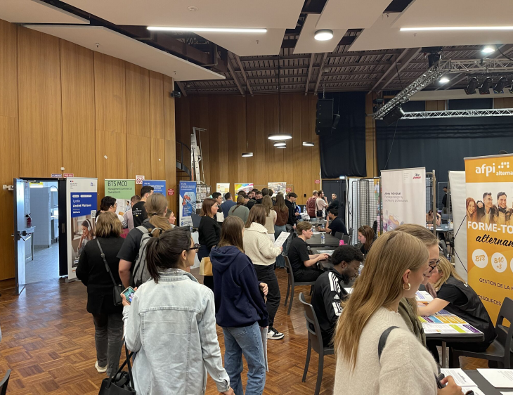 Forum dédié à l’alternance, se tenant dans une grande salle. De nombreux visiteurs, principalement des jeunes, échangent avec des exposants répartis sur des stands d’information